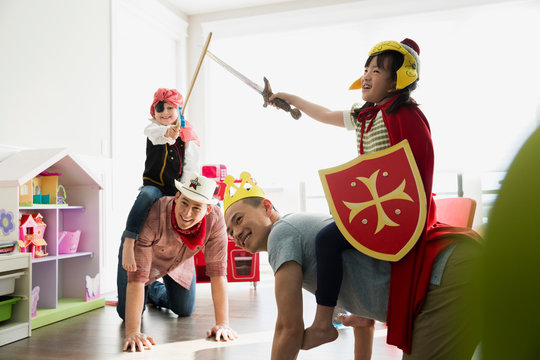Fathers piggybacking daughters in costumes playing sword fight