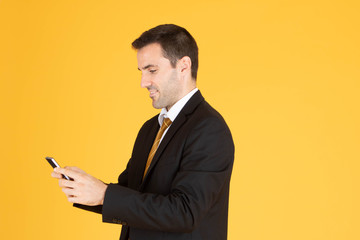Portrait of confident businessman using smartphone on yellow  background.