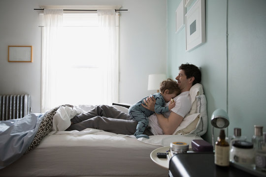 Father cuddling son in pajamas in bed