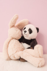 Plush panda and bunny hugging each other
