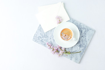 Fototapeta na wymiar Minimal elegant composition with coffee cup and lilac branches, envelope on white background, female morning breakfast, woman mother day, saint valentine day, wedding