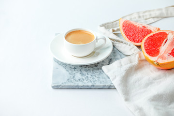 Flat lay coffee with eco craft tissue bag and grapefruit on marble plate and white background. Minimal stylish hipster concept, office desk, minimalism