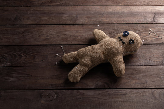 Voodoo doll on a wooden background with dramatic lighting. The concept of witchcraft and black art. Burlap doll on a wooden background. Pierce with maces. Copy space.