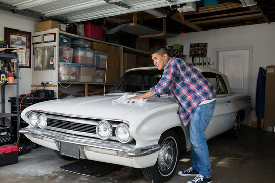 Young man waxing vintage car in garage