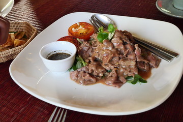 Cambodian Fried marinated beef flavor(( Lok Lak ) with sliced tomato in white plate on red table