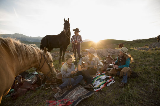 Female ranchers camping in remote field playing guitar