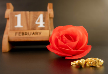 Celebration on valentine's day with red rose, wedding rings and wooden calendar on February 14 date, isolated on dark background. Concept of love and romance.