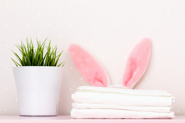A close-up of a stack of clean white bedding, Easter bunny ears and a houseplant, on a dressing...