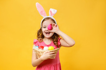 Happy child in the ears of a bunny holds an Easter egg and a basket. Portrait of a little girl on a...