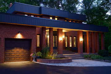 Front of a red brick house at twilight with pond and stone porch