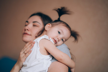 Young mother holding her little child girl. Daughter sleeping on mothers shoulder, care and love, unfocused photo, focus on hands.