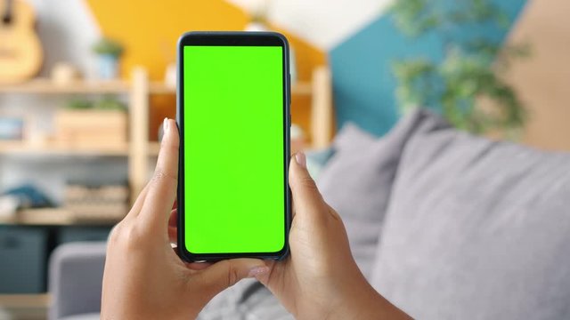 Close-up shot of green screen template smartphone in female hands at home, girl is watcing content without touching gadget screen. Modent technology and information concept.