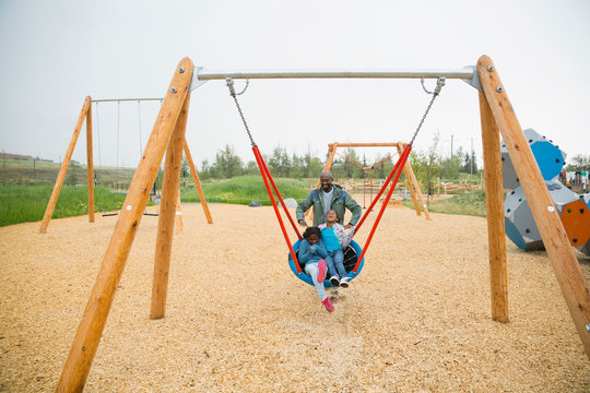 Father pushing daughters in swing net at playground