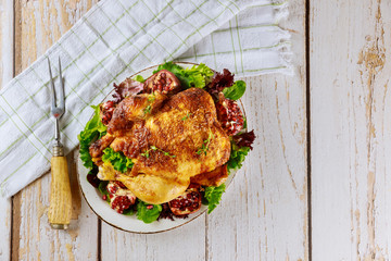 Whole roasted chicken on plate with salad, pomegranate and fork.