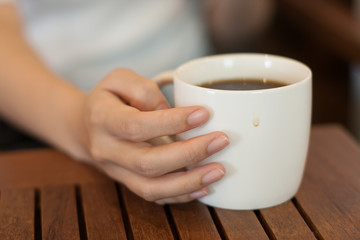 closeup woman hand holding a white cup of hot americano coffee on the table