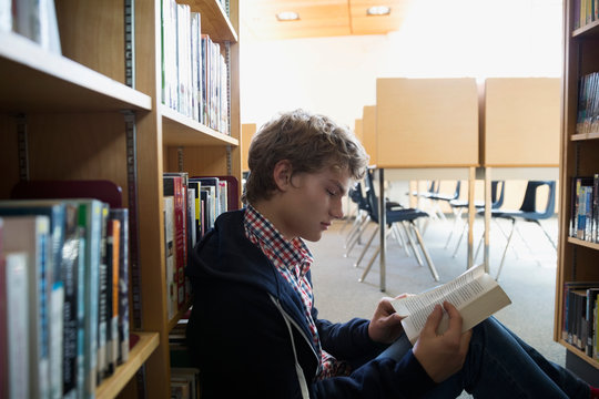 High School Student Reading Book On Library Floor