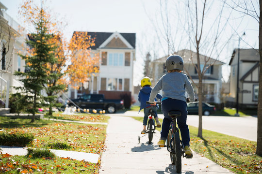Rear view boys riding bikes autumn neighborhood sidewalk