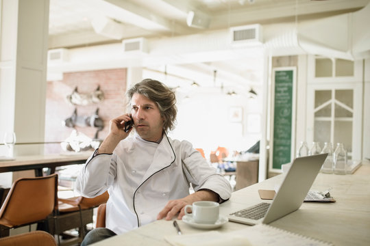 Chef talking on telephone at laptop in restaurant