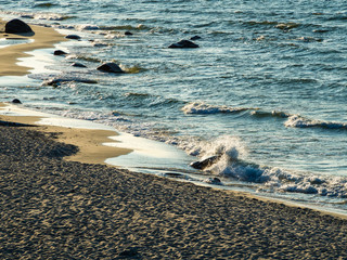 Sea waves with splashes at sunset or sunrise. Ocean waves washing coast sand beach at Baltic sea