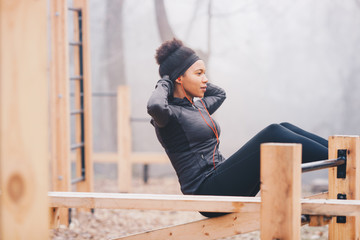 A woman doing sit-ups outdoors on an outdoor fitness equipment.