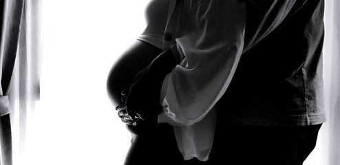 Silhouette of Close up husband's hand hug and touching wife's belly with white curtain background and left copy space in black and white tone. She is pregnant. New life and Lover family concept 