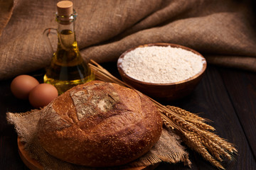 Loaf of bread on a wooden background, food closeup. Against the background of flour and vegetable oil with eggs.
