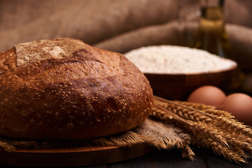 Loaf of bread on a wooden background, food closeup. Against the background of flour and vegetable oil with eggs.