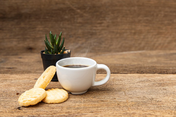 A white cup of coffee with cookie on the wooden table background.