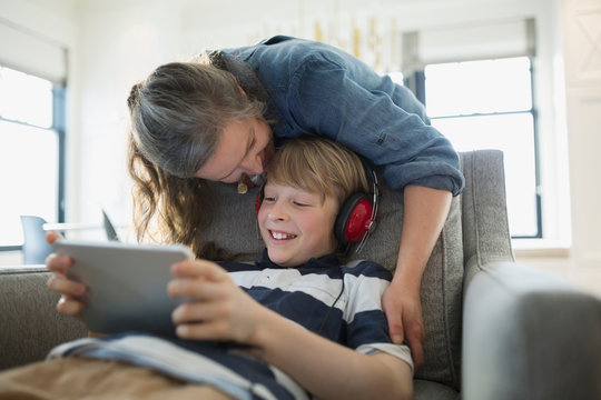 Mother kissing son with headphones using digital tablet