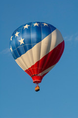 Fototapeta premium A red, white and blue-striped hot air balloon floats in a blue sky.