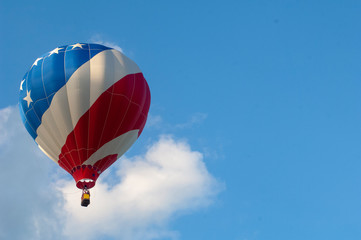 A red, white and blue-striped  hot air balloon floats in a blue sky with space for copy to the right.