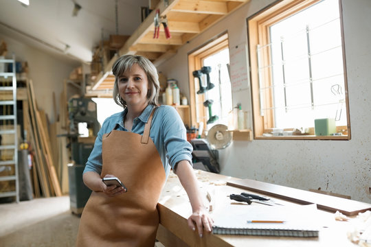 Portrait confident female carpenter with cell phone workshop