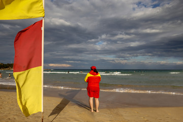 Red and yellow flags warning sign and   defocused female volunteer lifesaving beach patrol guard standing watching ensuring tourists swimming between flag on Australian beaches 