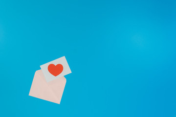 Fototapeta premium a red heart on a white paper, on pink envelope, put on the left of the picture on a blue background