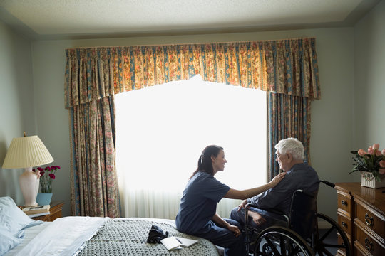 Home caregiver comforting senior man in wheelchair