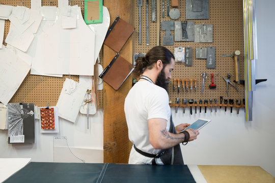 Leather worker using digital tablet at wall with tools