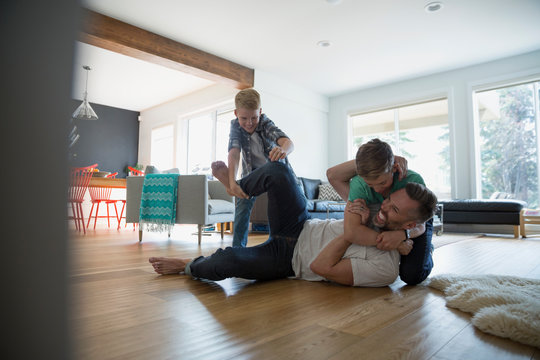 Father and sons rough housing on living room floor