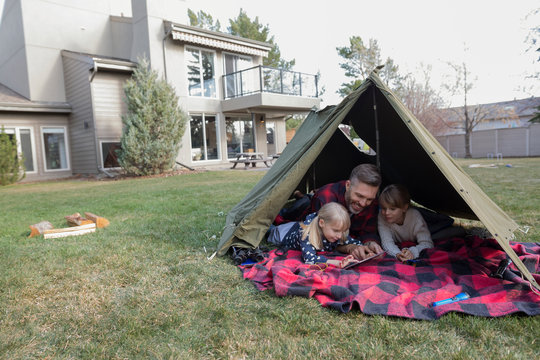 Father and daughters using digital tablet in backyard tent