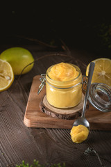 Lemon curd in glass jar with fresh lemons on wooden background