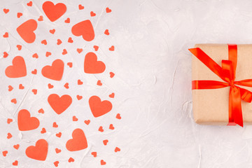 Valentine's Background with Gift Box with Red Ribbon Bow and Confetti Paper Hearts on Concrete Gray Background. Love, Romance, Happy Valentines Day Concept. Top View