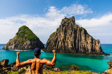 A tourist flexing muscles in front of Morro dos Dois Irmãos in Fernando de Noronha, Brazil. Solo...