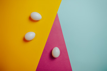 Happy Easter card with copy space. White eggs on colorful background. Orange, pink, blue paper background.