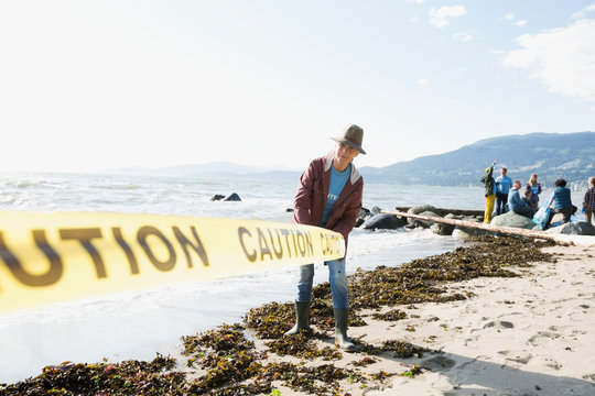 Beach cleanup volunteer rolling out caution tape on beach