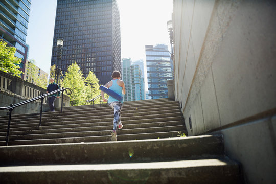 Woman with yoga mat ascending city steps