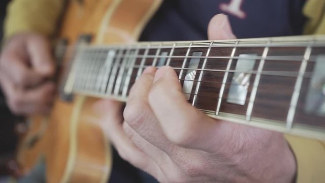 A close-up of a guitar master's hand sliding on the neck playing chords, scales and solos on a semi-acoustic hollow body guitar in natural light wood