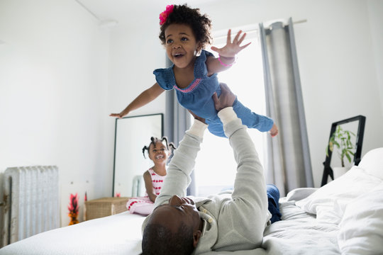 Father flying enthusiastic daughter overhead on bed