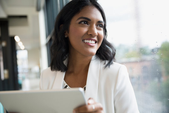 Portrait smiling businesswoman with digital tablet looking out office window