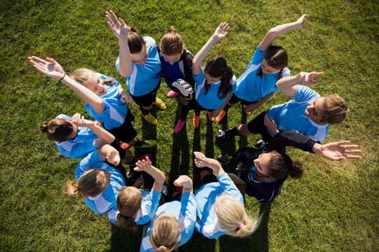 Overhead view middle school girl soccer team cheering in huddle with coach on field