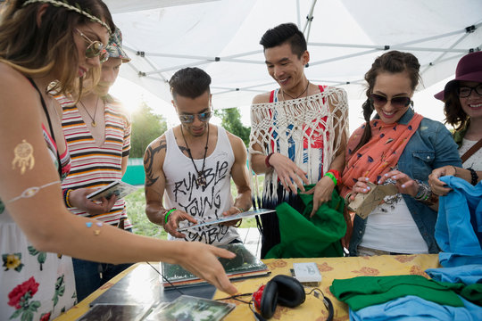 Young Friends Looking At Merchandise In Vendor Booth At Summer Music Festival