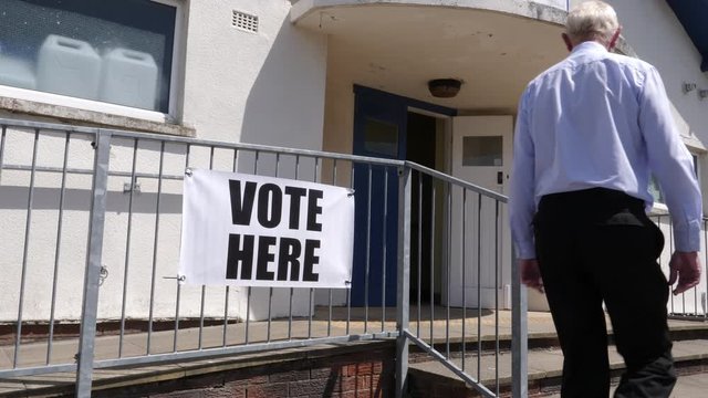 Vote here Sign - People walking past & going to vote in the election. Politics. 